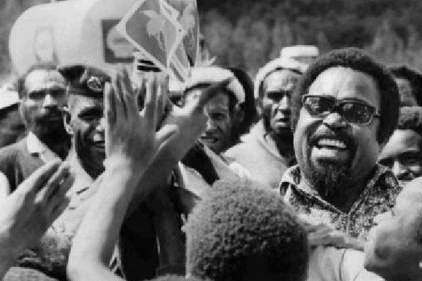 Sur cette photo de 1974, Sir Michael Somare, qui allait devenir le tout premier Premier ministre de la Papouasie Nouvelle-Guinée, agite le drapeau de son pays sur le point de devenir indépendant, en compagnie des élèves d'une école. (Denis Williams' estat