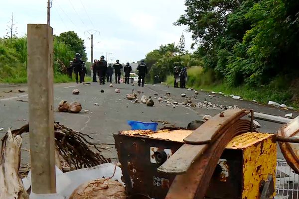 Présence de forces de l'ordre sur une route bloquée, obstruée par des déchets et des branches d'arbres, à Nouméa, ce 3 juin 2024