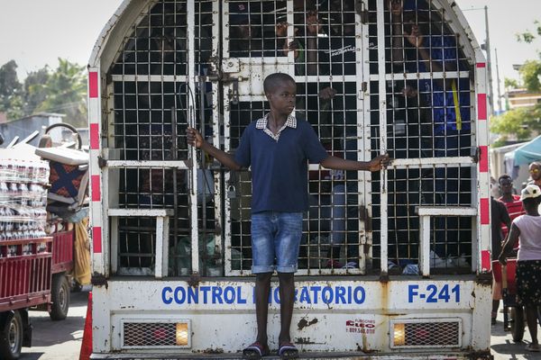 A la République-Dominicaine, un garçon se met debout sur le parechoc d'un camion à cage rempli d'immigrants d'Haïti.