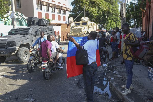 La police nationale haïtienne passe à proximité d'un homme brandissant un drapeau du pays, 20 septembre 2024