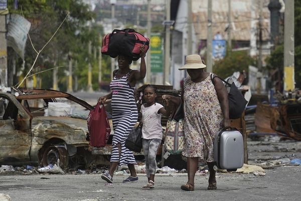 Des résidents passent devant une voiture brûlée bloquant la rue, alors qu'ils évacuent le quartier de Delmas 22, pour échapper à la violence des gangs à Port-au-Prince (Haïti).