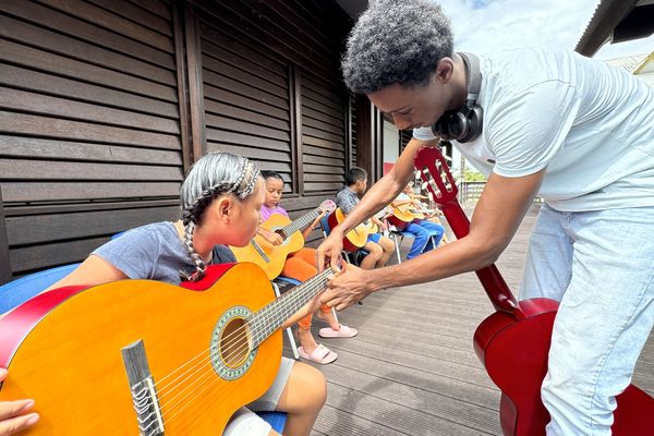 Une jeune fille reçoit des conseils pour accorder sa guitare pendant les ateliers de musique organisés par Ouest Guyane Animation.