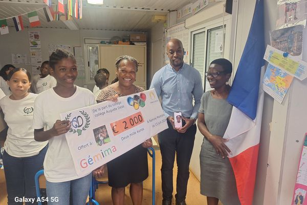 Une élève du collège Auguste Dédé remet le chèque récolté pour Gemima Joseph à son frère.